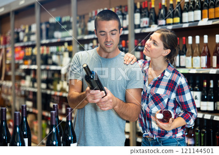 Married couple chooses wine in the alcohol department of supermarket Married couple chooses wine in the alcohol department of supermarket 121144501