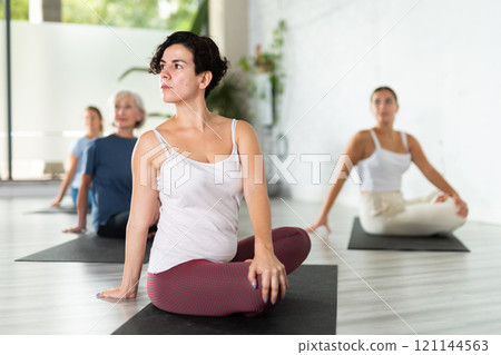 Portrait of women practicing Matsyendrasana known as Lord of Fishes Pose during group yoga training 121144563