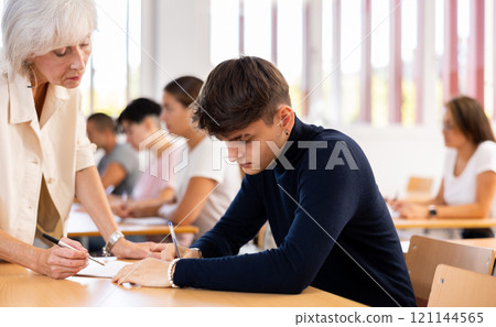 Female teacher helps student complete an assignment in university class 121144565