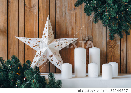 Holiday Christmas decor with white star, candles, and evergreen wreaths on wood background 121144837