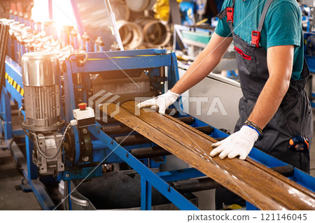 A factory worker is making a metal profile for a roof. Worker at factory measures metal profiled sheet. He works in metal production industrial. metal roofing production, production of roof elements 121146045
