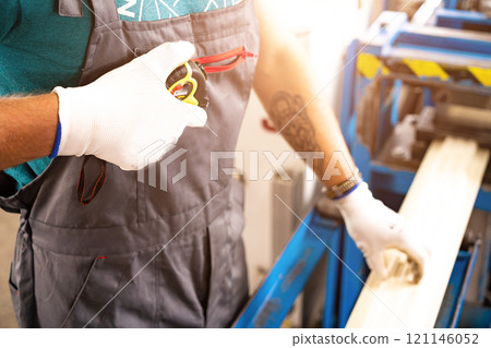 A factory worker is making a metal profile for a roof. Worker at factory measures metal profiled sheet. He works in metal production industrial. metal roofing production, production of roof elements A factory worker is making a metal profile for a roof. Worker at factory measures metal profiled sheet. He works in metal production industrial. metal roofing production, production of roof elements 121146052