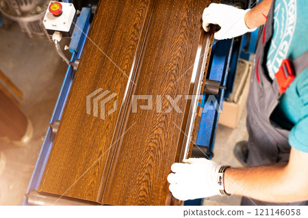 A factory worker is making a metal profile for a roof. Worker at factory measures metal profiled sheet. He works in metal production industrial. metal roofing production, production of roof elements A factory worker is making a metal profile for a roof. Worker at factory measures metal profiled sheet. He works in metal production industrial. metal roofing production, production of roof elements 121146058