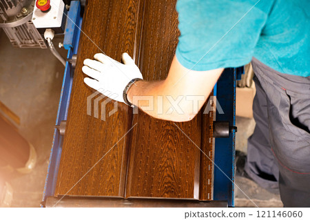 A factory worker is making a metal profile for a roof. Worker at factory measures metal profiled sheet. He works in metal production industrial. metal roofing production, production of roof elements A factory worker is making a metal profile for a roof. Worker at factory measures metal profiled sheet. He works in metal production industrial. metal roofing production, production of roof elements 121146060
