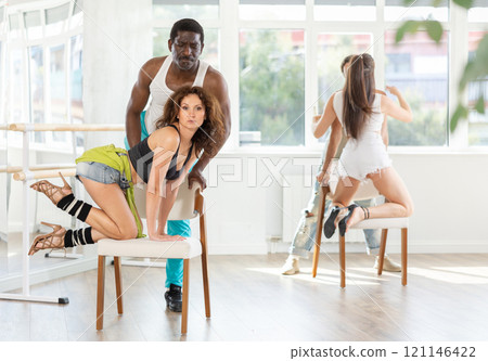 Woman in heels dances with man kneeling on chair Woman in heels dances with man kneeling on chair 121146422