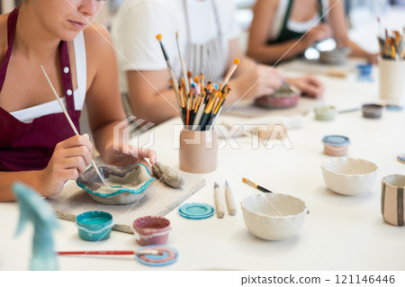 Close up girl paints bowl of clay during master class, top view. 121146446