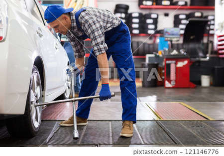 Mechanic engaged in replacement of tyre on car wheel in workshop 121146776