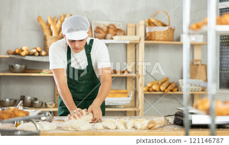 Young male baker kneads the dough in bakery 121146787