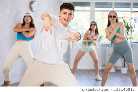 Male teen teacher with young girls in dark glasses and ball cap dance Jazz-modern at lesson Male teen teacher with young girls in dark glasses and ball cap dance Jazz-modern at lesson 121146812