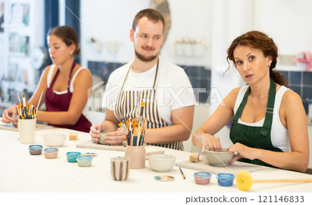 Three students in pottery workshop learn to create homemade plates and other utensils 121146833