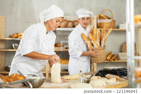 Young female baker kneading dough on floury table in artisan bakery 121146841