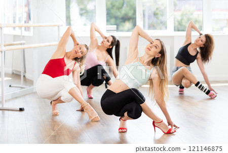 Girls with women perform dance in heels, squat down, actively repeat movements of instructor. 121146875