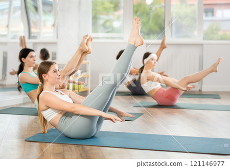 Young female participant working out Paripurna Navasana, boat pose with students group Young female participant working out Paripurna Navasana, boat pose with students group 121146977