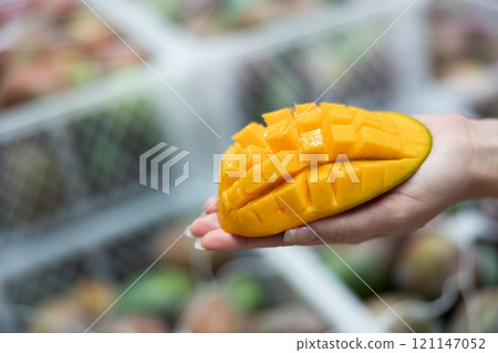 Fresh sliced mango on hand, blurred boxes with fruits on background Fresh sliced mango on hand, blurred boxes with fruits on background 121147052