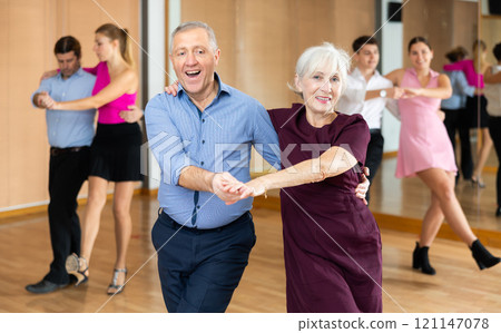 Cheerful elderly couple practicing ballroom dances in ballroom 121147078