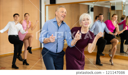 Cheerful elderly couple practicing ballroom dances in ballroom 121147086