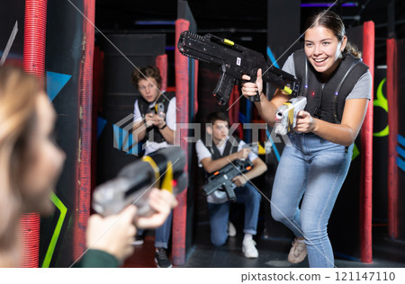 Smiling girl with laser pistol during playing laser tag with her friends in room 121147110