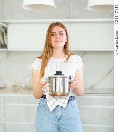 Portrait of teen girl holding small pot in her hands after cooking in cozy kitchen Portrait of teen girl holding small pot in her hands after cooking in cozy kitchen 121147118