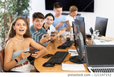 At computer class, young girl student sits with mobile phone and listens admiringly to teacher At computer class, young girl student sits with mobile phone and listens admiringly to teacher 121147152