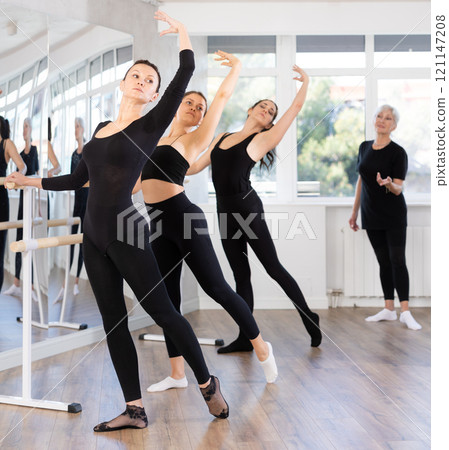 Female ballet trainer teaching group of dancers near ballet barre in dancing studio 121147208
