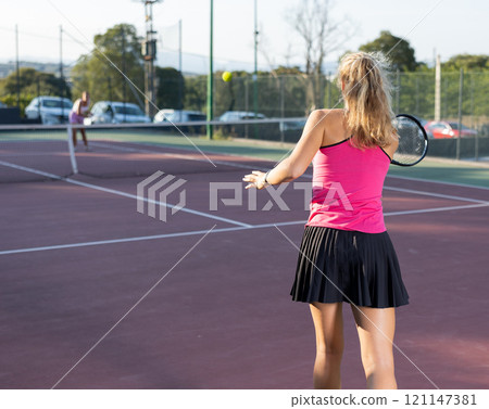 Rear view of woman playing tennis match on court on blurred background of opponents. Sport and active lifestyle concept Rear view of woman playing tennis match on court on blurred background of opponents. Sport and active lifestyle concept 121147381