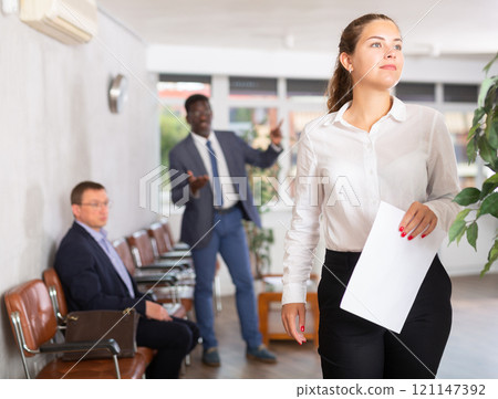 Upset young woman with documents standing in reception 121147392