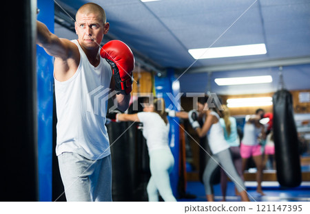 Man practicing boxing punches in gloves on punching bag 121147395