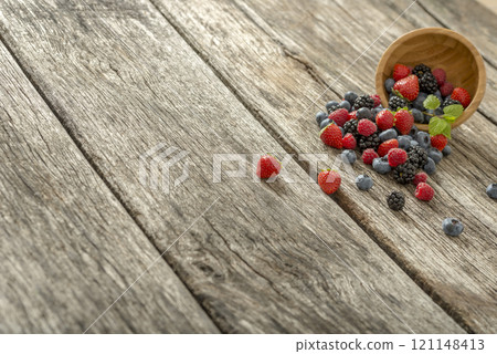 Delicious berry fruits, strawberries, blueberries, raspberries, blackberries, scattered from a wooden bowl 121148413