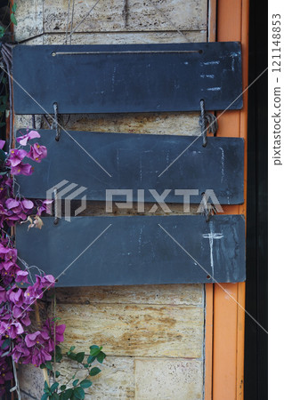 An empty chalkboard sign adorned with lovely vines that is placed against a stone wall 121148853