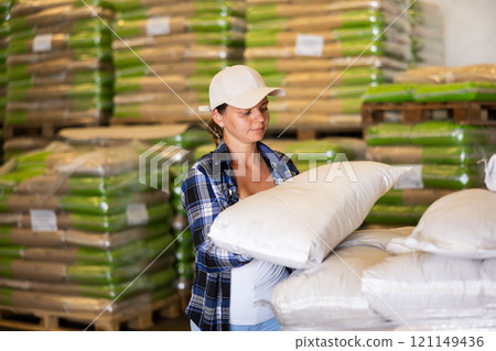 Woman working in warehouse, lifting heavy bag 121149436