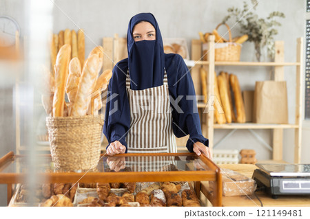 Muslim woman in apron behind pastry counter 121149481