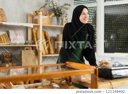 Girl seller of an oriental bakery in traditional muslim clothes with fresh hot croissants in hands 121149492