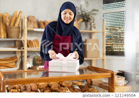 Saleswoman in a hijab holds a box with a bow 121149504