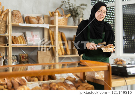 European Muslim woman seller in hijab weighs croissants on scale, European Muslim woman seller in hijab weighs croissants on scale, 121149510