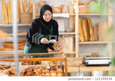 Girl seller of an oriental bakery in traditional muslim clothes with fresh hot croissants in hands Girl seller of an oriental bakery in traditional muslim clothes with fresh hot croissants in hands 121149534