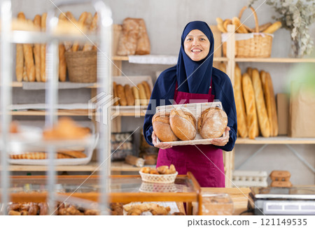 Middle-aged Muslim saleswoman displays sourdough bread in wicker basket Middle-aged Muslim saleswoman displays sourdough bread in wicker basket 121149535