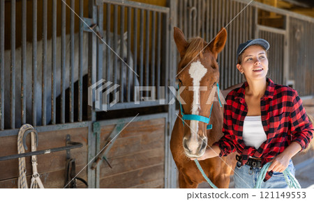 Young woman leads horse out of stable 121149553