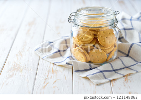 Full jar of delicious wheat round crackers on a white table, with copy space for text.  Close-up of a jar full of saltine round crackers . 121149862