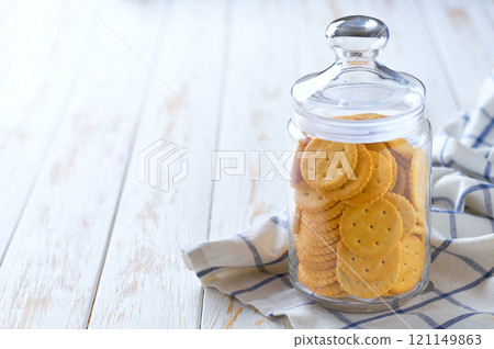 Saltine round crackers in a jar, on a light kitchen table, with copy space for text. Glass jar with wheat round crackers on a white table. Saltine round crackers in a jar, on a light kitchen table, with copy space for text. Glass jar with wheat round crackers on a white table. 121149863