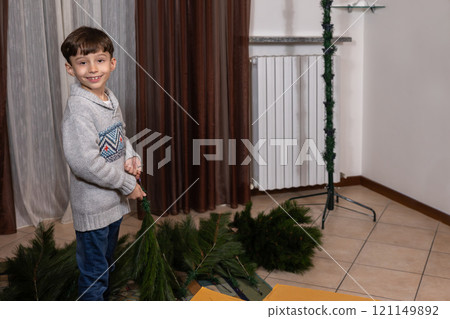 Young caucasian boy assembling artificial christmas tree at home. 121149892
