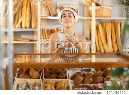 Young saleswoman holds out croissants in plastic bag in bakery Young saleswoman holds out croissants in plastic bag in bakery 121150521