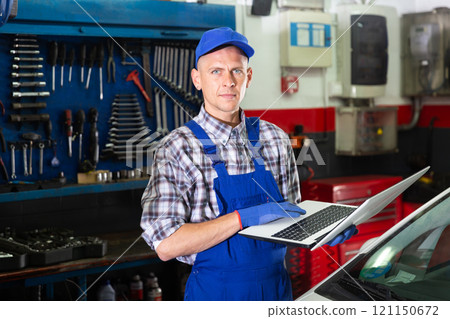 Mechanic man using laptop checking car in workshop 121150672