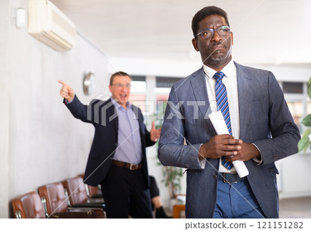 Angry hot-tempered boss shouts yells at hired employee African man in office reception. Angry hot-tempered boss shouts yells at hired employee African man in office reception. 121151282