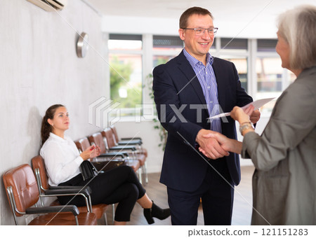 Middle-aged man handshaking with other person in waiting room Middle-aged man handshaking with other person in waiting room 121151283