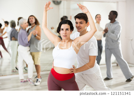Smiling guy supporting focused Latina practicing ballet dance moves 121151341