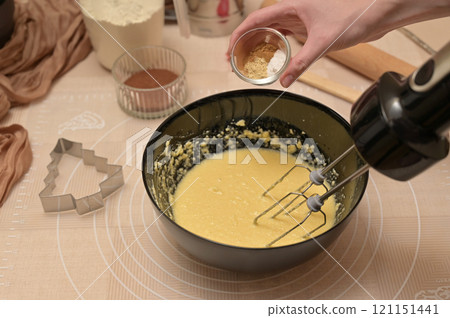 Christmas homemade baking, ingredients for baking gingerbread, woman adding spices to dough in black bowl Christmas homemade baking, ingredients for baking gingerbread, woman adding spices to dough in black bowl 121151441