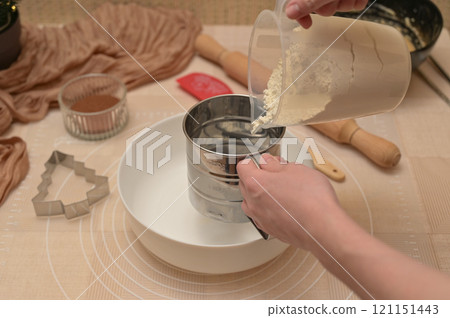 Christmas homemade baking, ingredients for baking gingerbread, woman sifting flour in a white bowl 121151443
