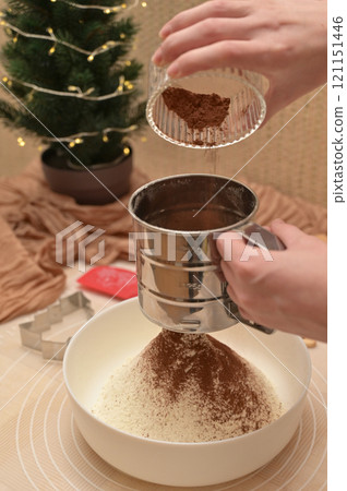 Christmas homemade baking, ingredients for baking gingerbread, woman sifting cocoa in a white bowl 121151446