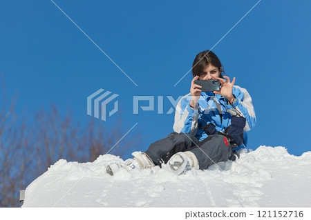 Female skier sitting on a roof taking picture with phone Female skier sitting on a roof taking picture with phone 121152716