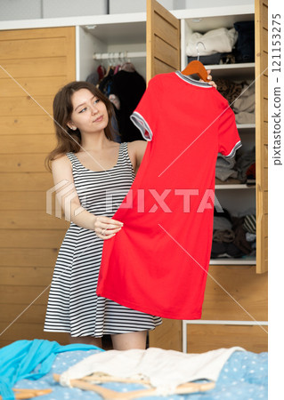 Young woman choosing which dress to wear Young woman choosing which dress to wear 121153275